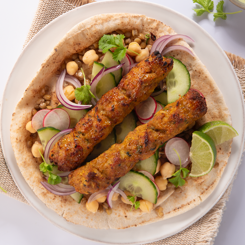 Chicken sheesh kebabs on a paratha with vegetables, accompanied by a small bowl of green sauce.