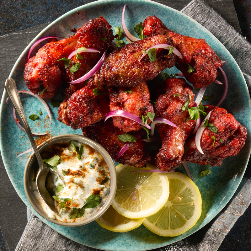 Plated dish of grilled chicken wings with lemon slices and a small bowl of dipping sauce.